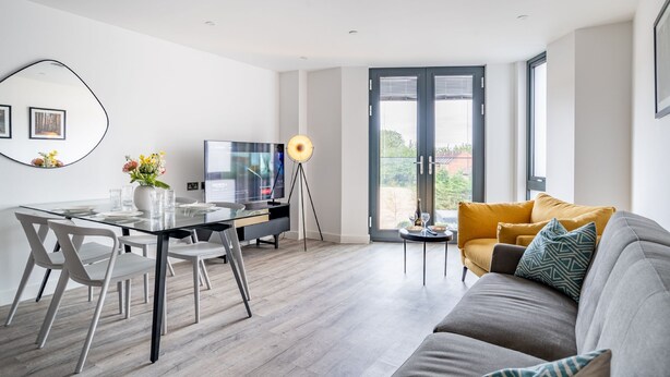 A modern living room with a grey sofa, a glass dining table, and a TV. - 42 City Gate - 24-hour Gym Access Included! Sleeps 4 guests in 2 bedrooms (York)
