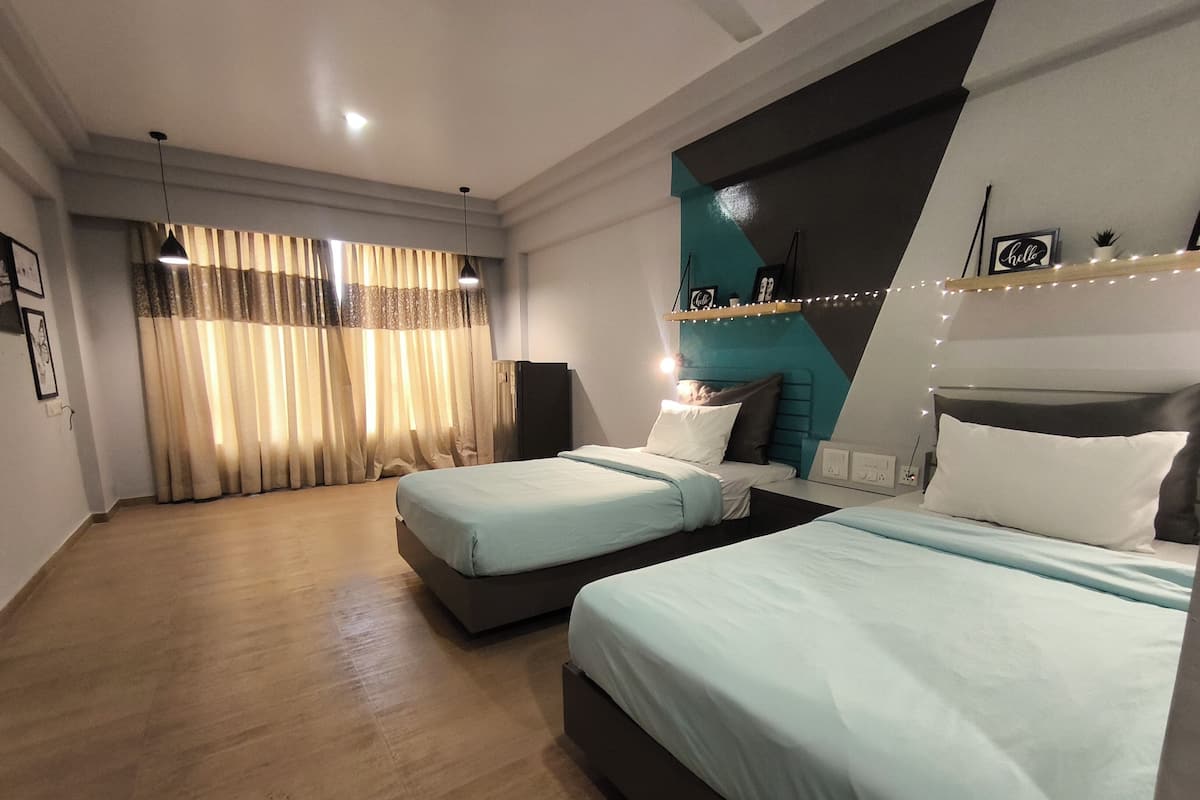 A modern hotel room with two beds, a large window with curtains, a teal accent wall, and a string of lights.