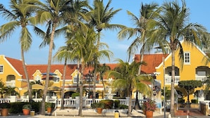 A yellow building with a red roof, surrounded by palm trees and potted plants.