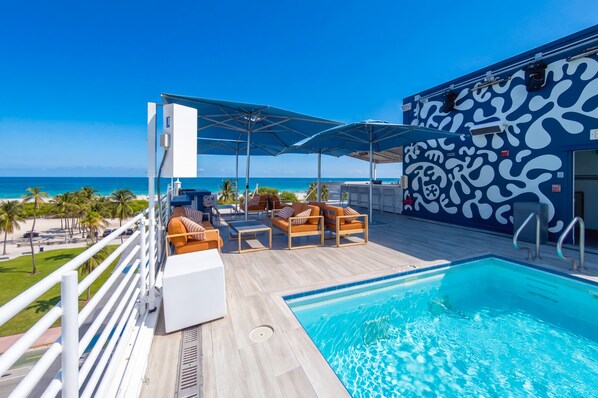 A poolside area with lounge chairs and umbrellas, a pool, and a view of the ocean.