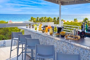 A bar area with a view of the ocean, bar stools, and a variety of drinks.