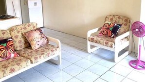 Ein Wohnzimmer mit zwei blumigen Sofas, einem kleinen Tisch und einem pinken Ventilator.