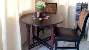 Ein runder Holztisch mit dunkler Oberfläche, begleitet von einem dunkel gepolsterten Stuhl. Auf dem Tisch steht ein kleiner Strauß mit weißen Blumen.