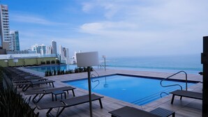 A rooftop pool area with lounge chairs and a view of the ocean and city skyline. - Relax in front of the sea (Cartagena de Indias)