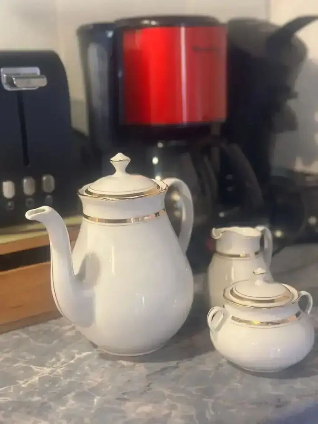A kitchen area with a white teapot, a smaller teapot, and a red coffee maker on the counter.