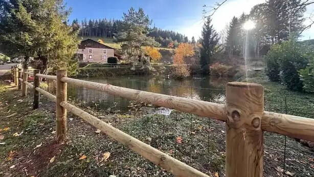 Ein Holzzaun mit Blick auf einen Fluss, im Hintergrund ein Haus.