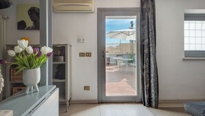 A room with a sliding glass door leading to an outdoor patio area, a white radiator, a white vase with flowers, and a grey sofa. - British Embassy Terrace Apartment (Rome)