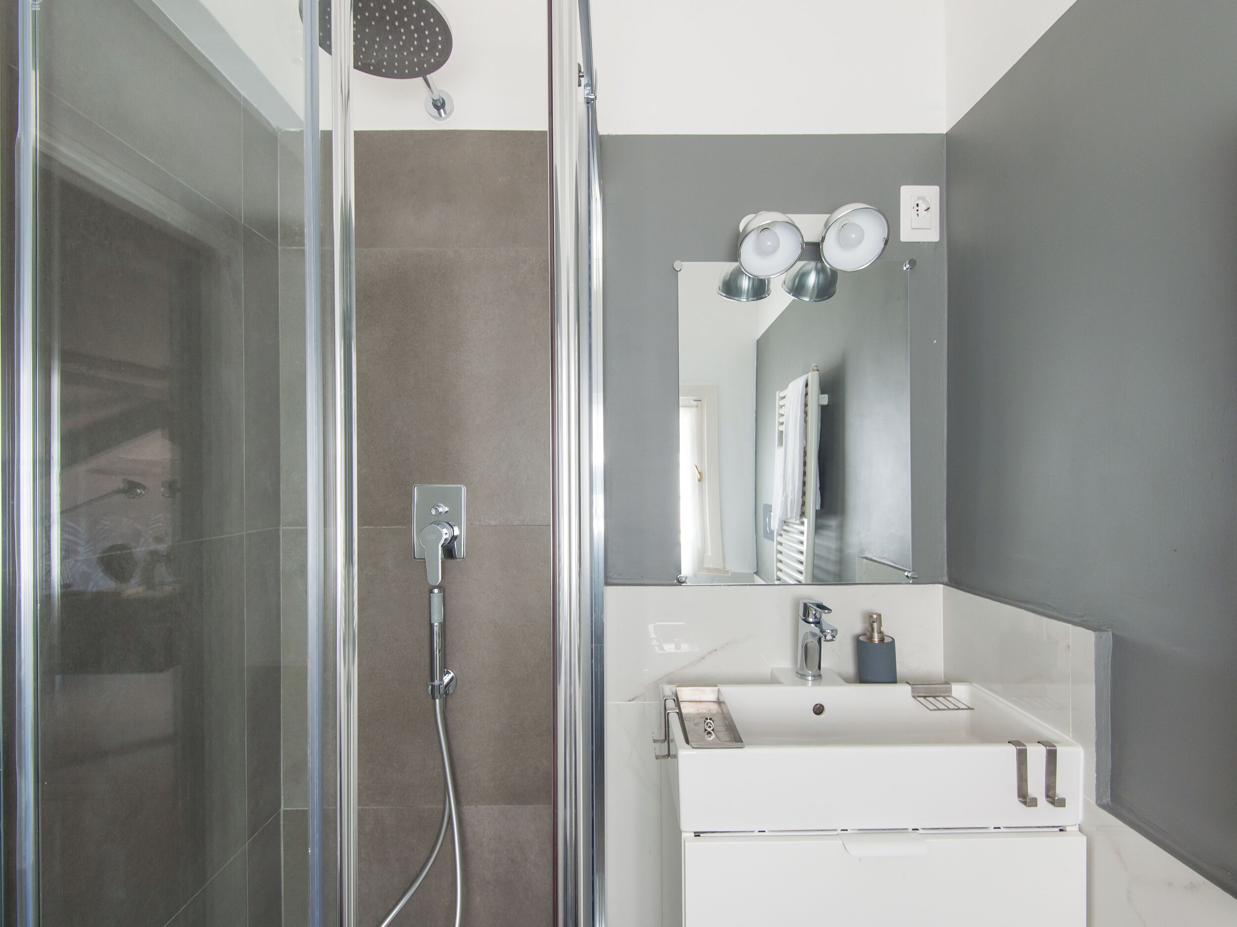 Une salle de bain moderne avec une douche à parois de verre, un lavabo blanc et un miroir au-dessus.