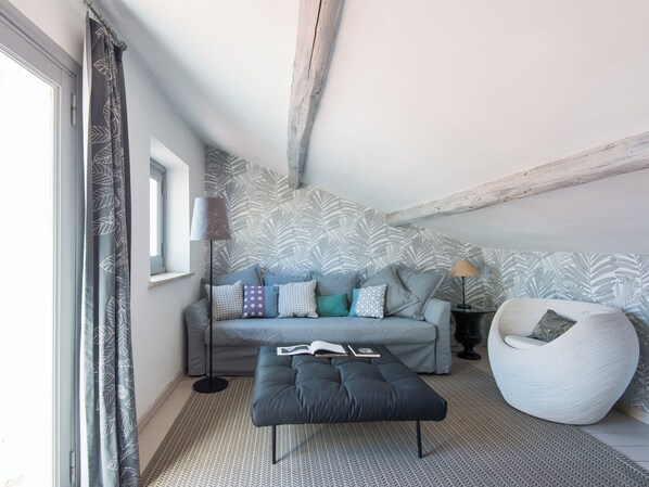 A modern loft bedroom with a grey sofa, patterned wallpaper, and a large window. - British Embassy Terrace Apartment (Rome)