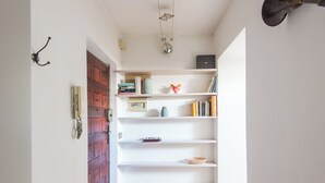 A hallway with a wooden door, white shelves with books and decorative items, and a hanging light fixture. - British Embassy Terrace Apartment (Rome)