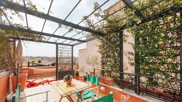 Un patio al aire libre con una mesa y sillas, rodeado de macetas con plantas y una pérgola.