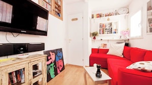 Una sala de estar con un sofá rojo, un televisor de pantalla plana, una estantería y un cuadro.