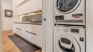 A modern kitchen with white cabinets, a stainless steel range hood, and a built-in washer and dryer unit.