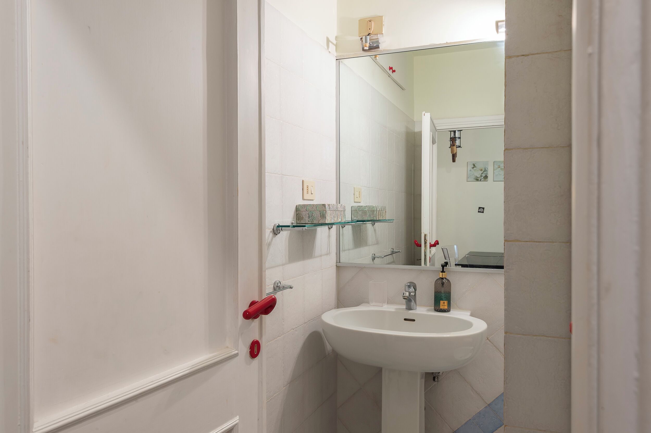 Een badkamer met een wit wastafel, glazen planken en een spiegel.