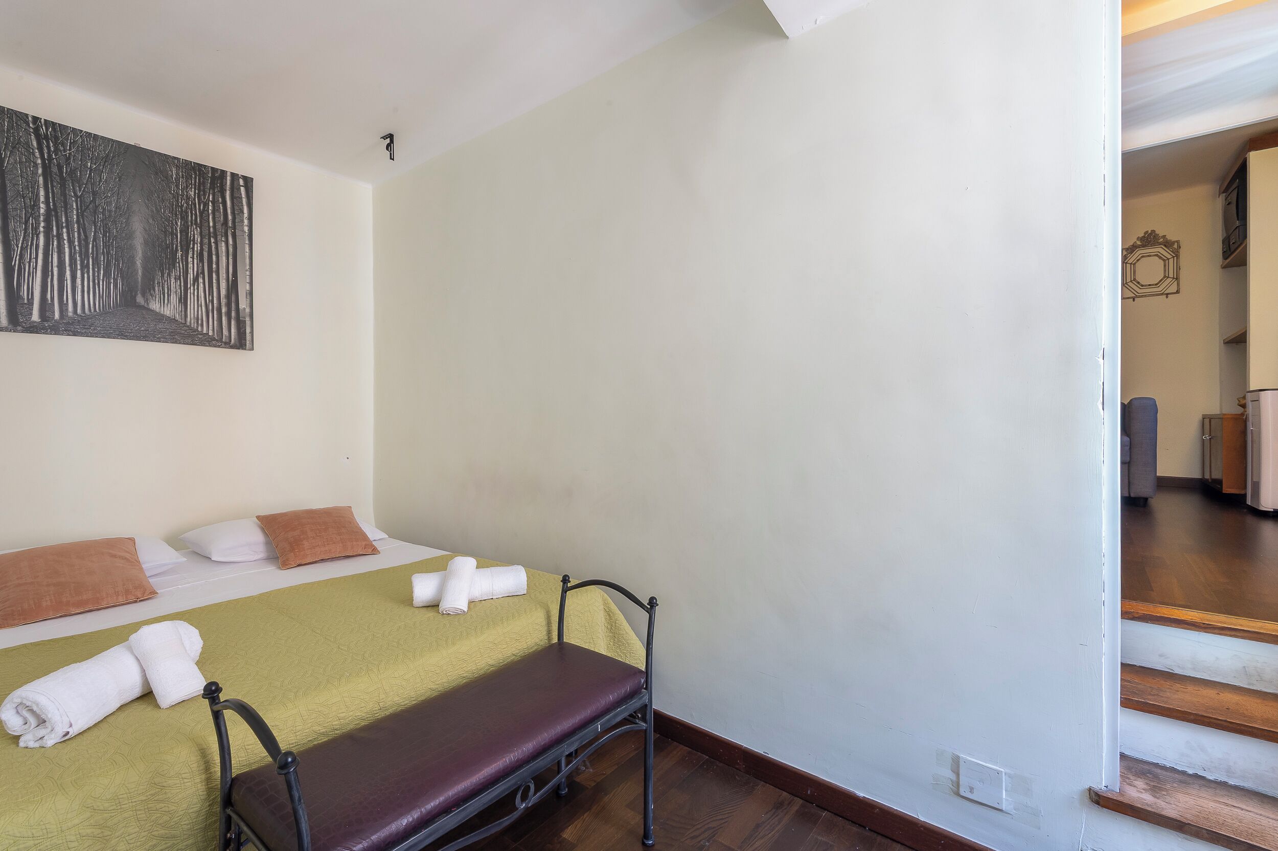 Une chambre d’hôtel avec deux lits, l’un recouvert d’une couvre-lit verte et l’autre d’une couvre-lit marron. Un tableau est accroché au mur au-dessus des lits, et un escalier mène à une autre partie de l’hôtel.