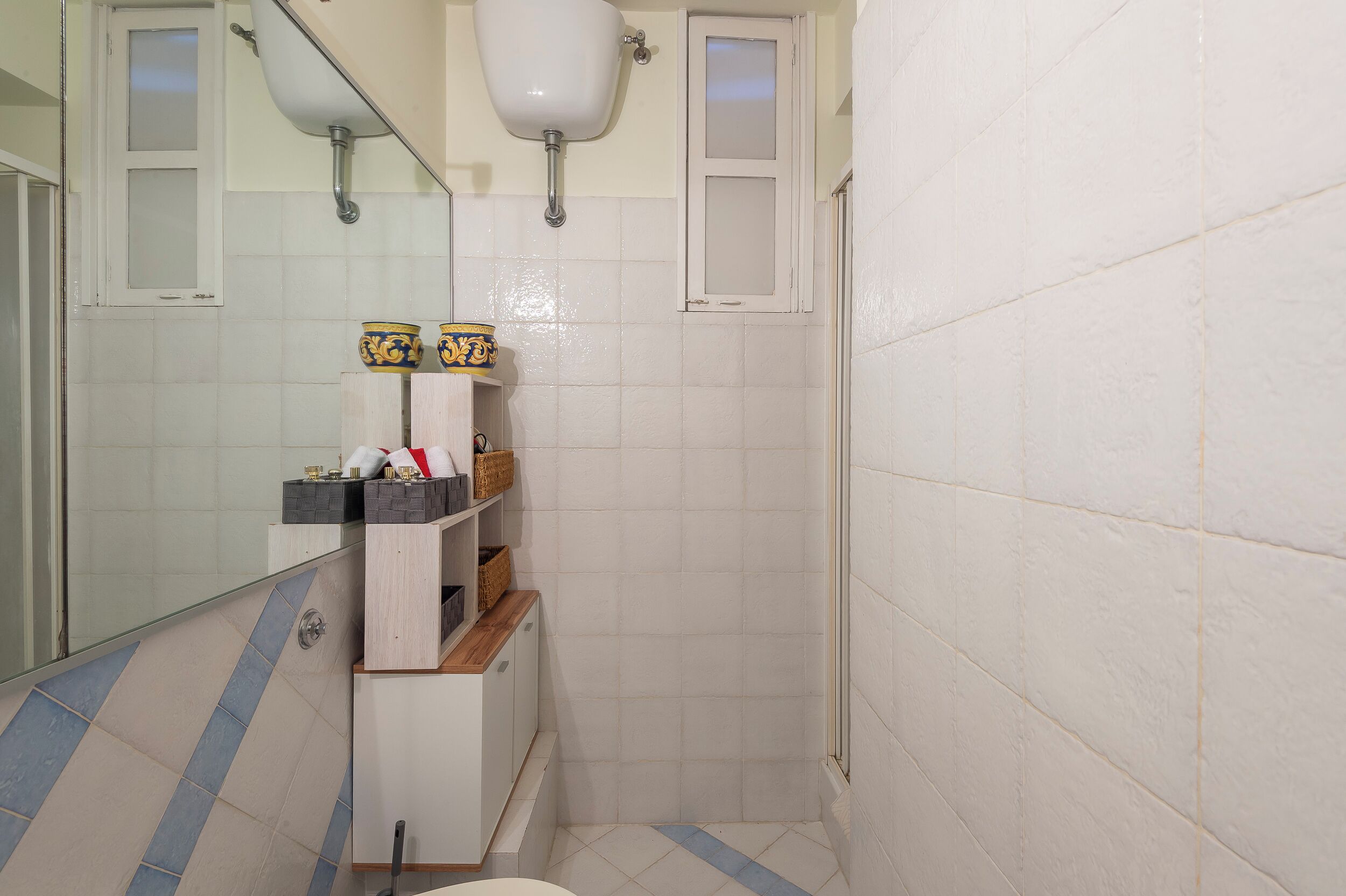 A bathroom with white tiled walls, a mirror, a sink, and a shower area.