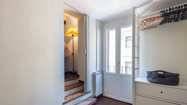 Un couloir avec un escalier en bois, un radiateur et une porte blanche donnant sur un balcon.