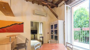 A dining area with a wooden table and metal chairs, a painting on the wall, and a view of greenery outside. - Charming Luxury Trastevere Apartment (Rome)