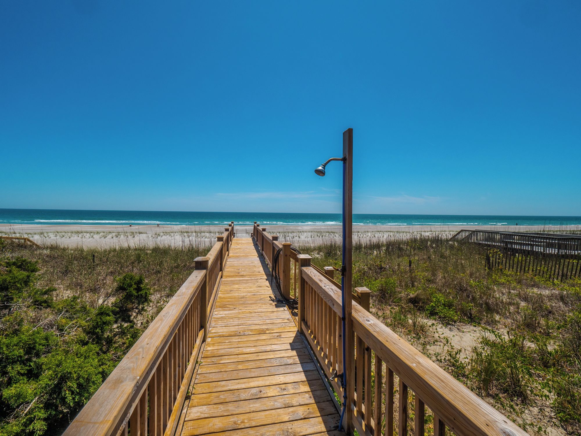 Un paseo marítimo de madera que lleva a una playa, con una vista despejada del océano.