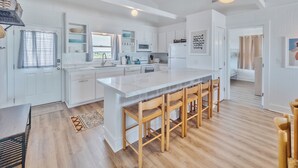 A modern kitchen with white cabinetry, a large island with bar stools, and a view to the dining area.