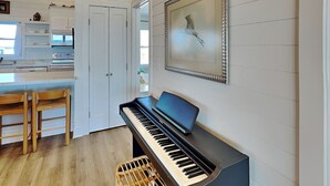 Ett piano i ett rum med trägolv, en vit dörr och en inramad tavla på väggen.