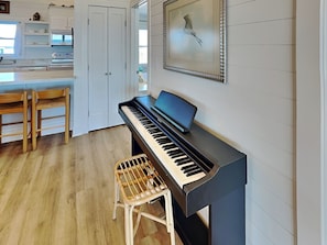 A piano in a room with a wooden floor, a white door, and a framed picture on the wall. - Walking on Sunshine by Topsail Realty (Holly Ridge)