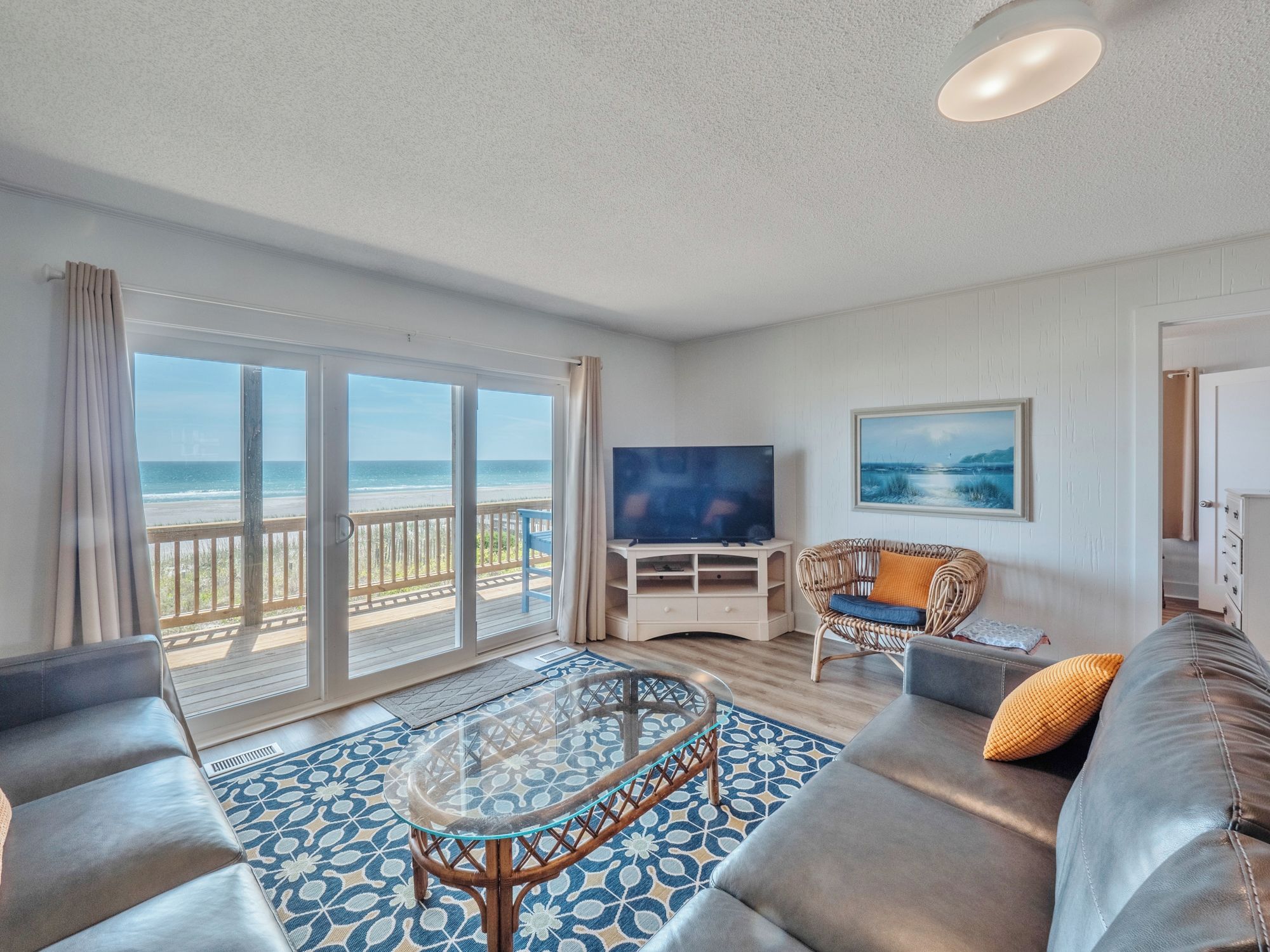 A spacious living room with a large sliding glass door leading to a balcony with a view of the beach.