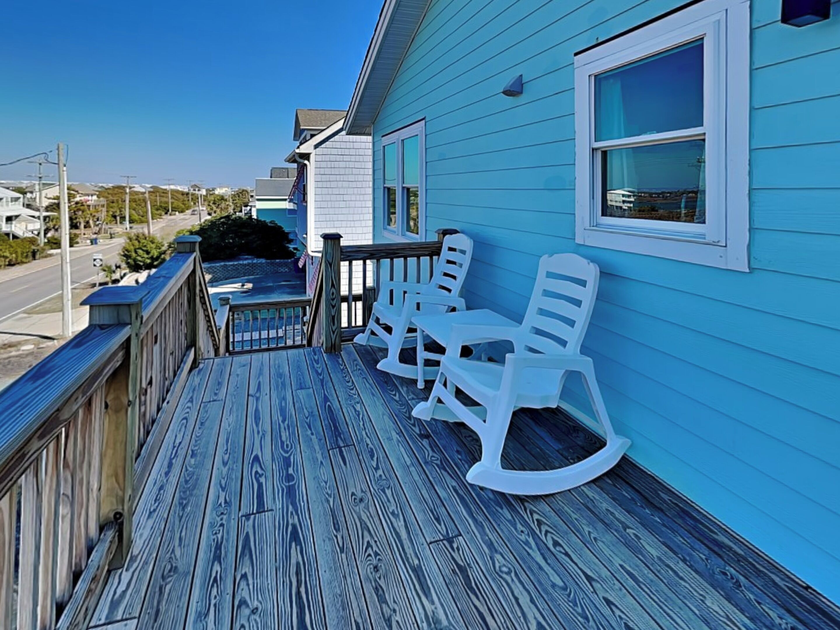 A blue house with a wooden deck, white rocking chairs, and a small table.
