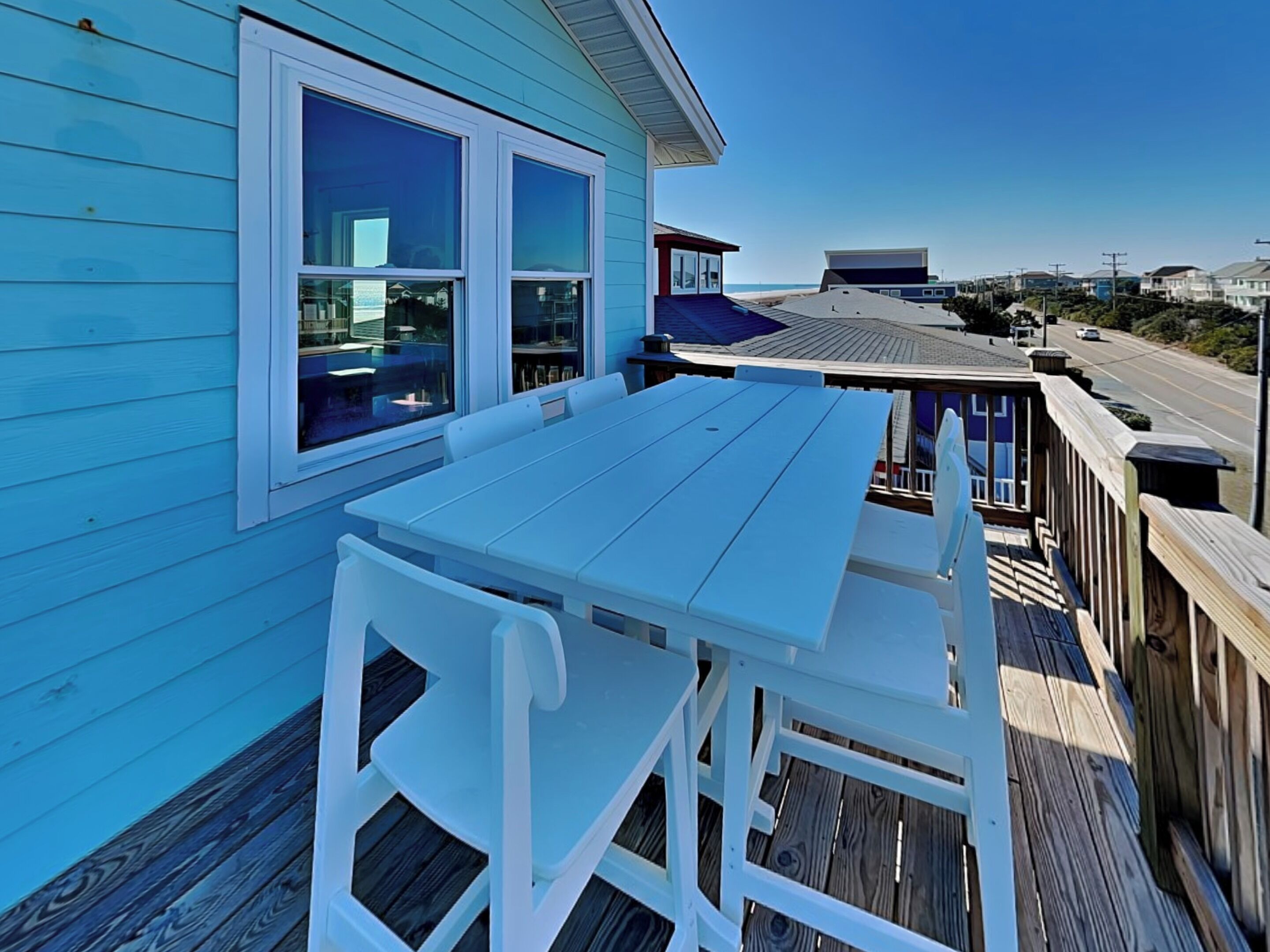 A blue house with a deck, white outdoor furniture, and a view of the beach and ocean.