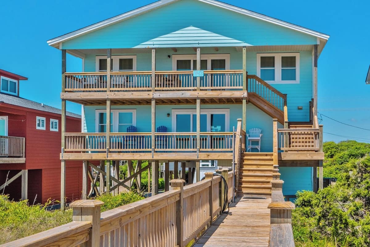 Casa frente al mar de dos pisos con terraza de madera y balcón.