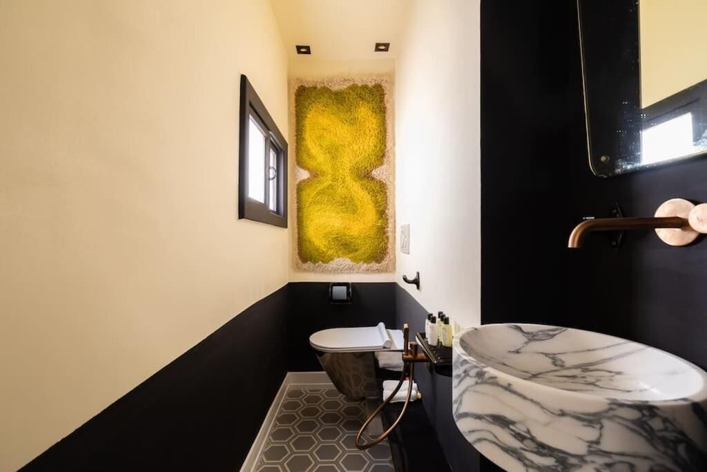 Une salle de bain moderne aux couleurs noir et blanc, avec un mur à la texture originale, un sol carrelé en forme d’hexagone et un lavabo en marbre.