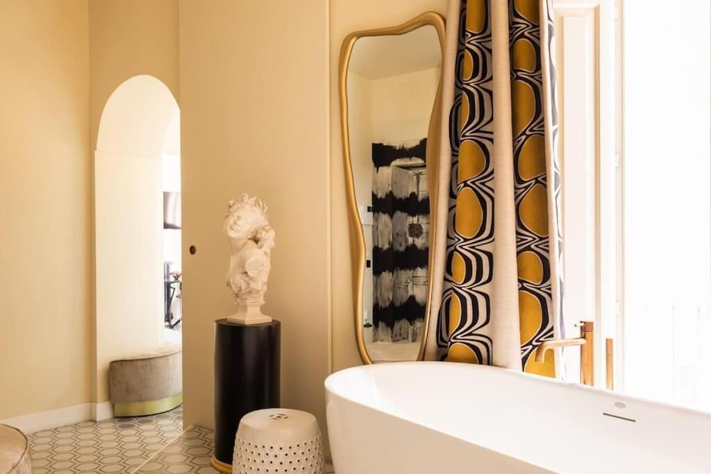 A bathroom with a white bathtub, a large mirror with a gold frame, and a statue on a pedestal.