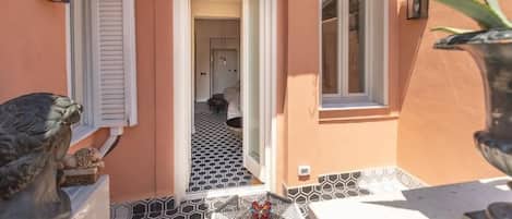 A narrow outdoor corridor with a tiled floor, a door leading to an interior space, and a small table with a decorative item.