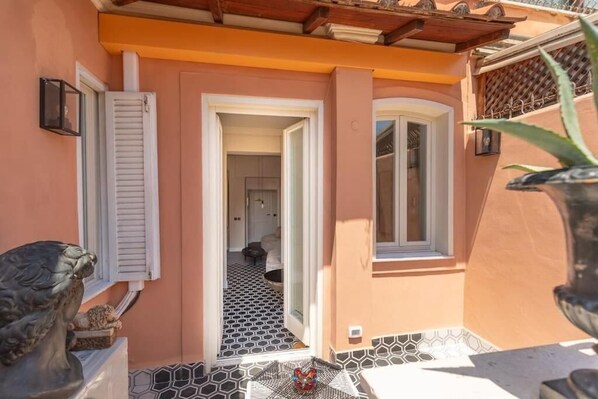 A narrow outdoor corridor with a tiled floor, a door leading to an interior space, and a small table with a decorative item. - Via Veneto Supreme Terrace (Rome)