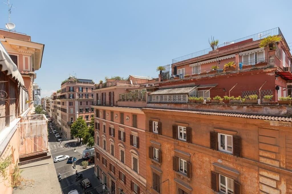 A narrow street lined with multi-story buildings, featuring balconies with plants and a clear sky.