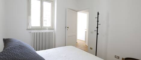 Ett sovrum med en säng, ett element, ett fönster och en dörr som leder till ett annat rum.