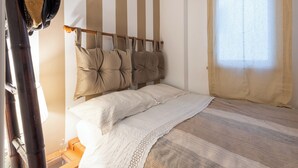 A bedroom with a bed, striped wall, hanging light bulbs, and a window.