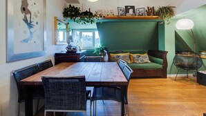 A dining area with a wooden table and chairs, a green sofa, and a hanging plant.