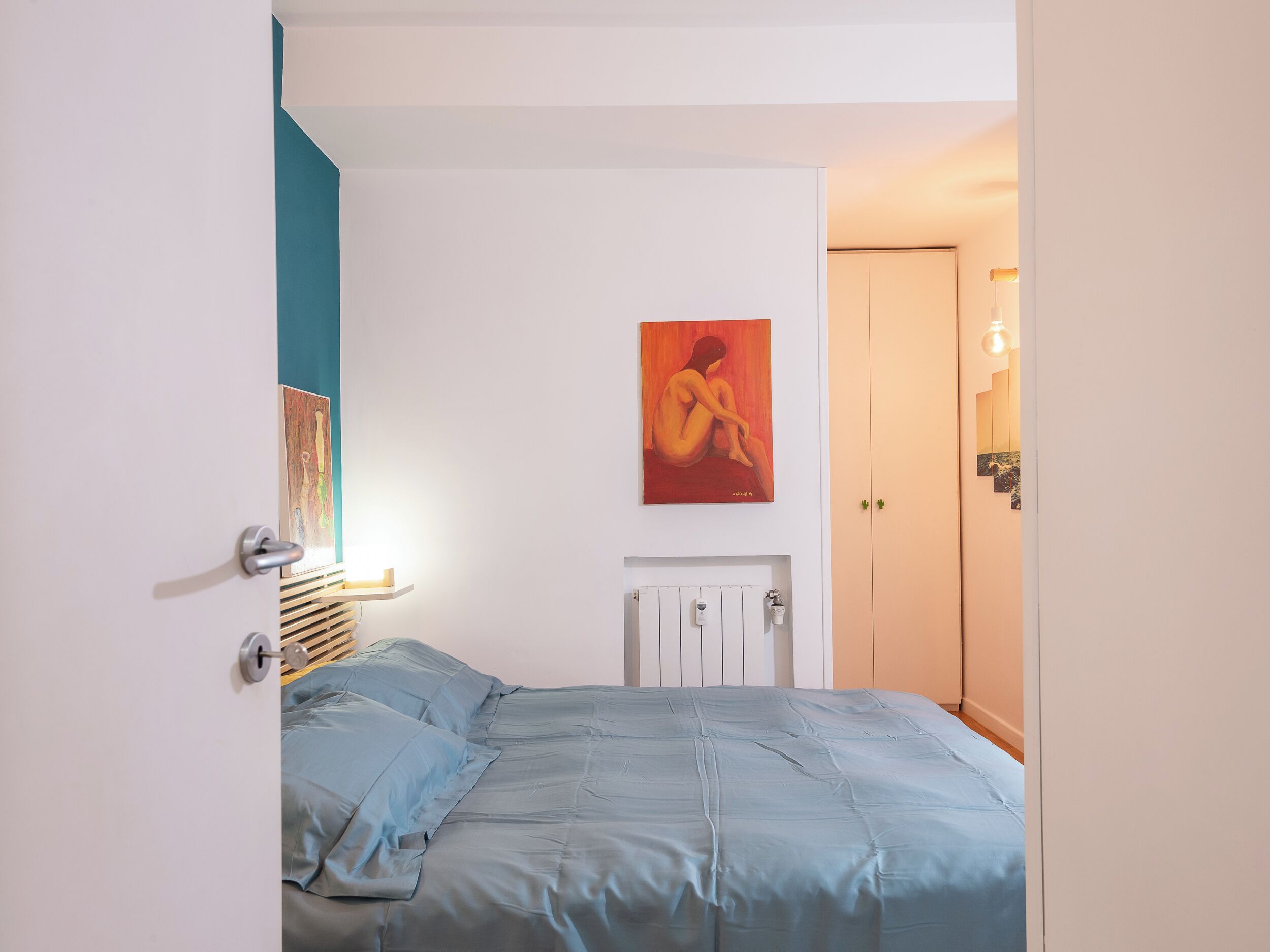 A bedroom with a bed, a radiator, a painting, and a door.