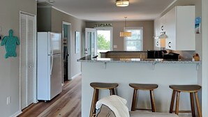 Une cuisine moderne avec un îlot central, des tabourets en bois et un réfrigérateur.