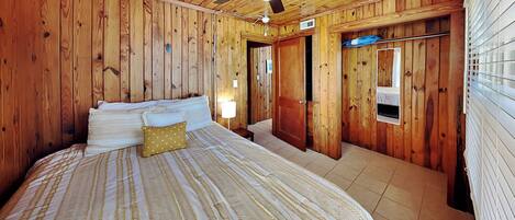 A wooden-paneled room with a bed, a ceiling fan, and a window with blinds.