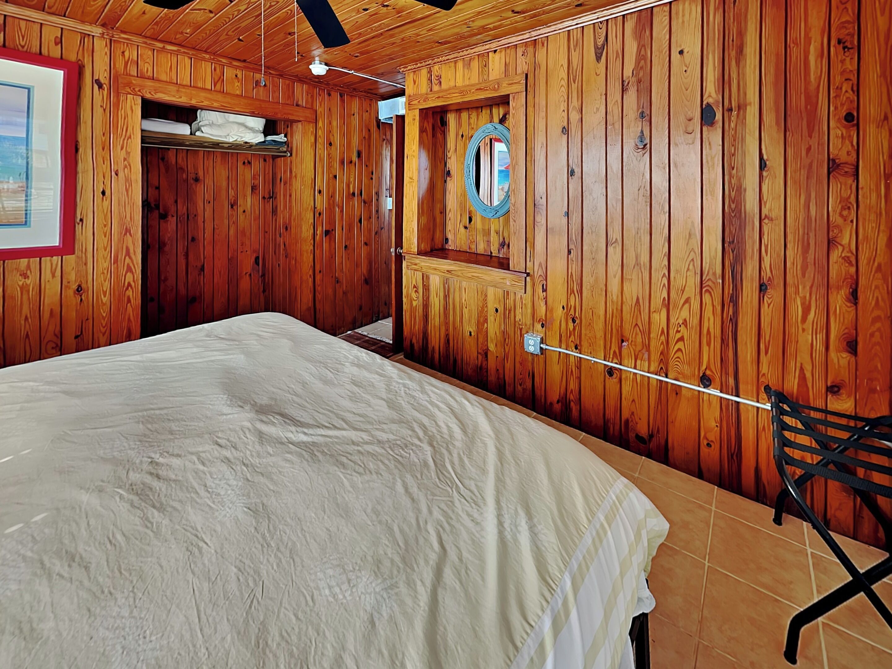 A wooden-paneled room with a bed, a small table, and a chair.