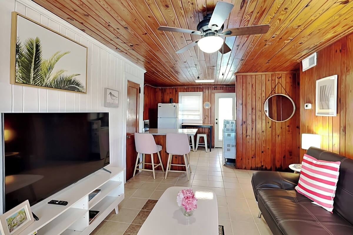 A cozy living room with a flat-screen TV, a coffee table with flowers, a leather sofa, and a dining area with a white table and chairs.