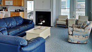 Uma sala de estar com um sofá azul, uma poltrona estampada e uma lareira.