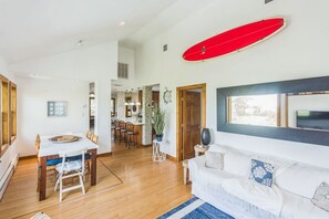 A spacious living area with a dining table, a sofa, and a red surfboard.