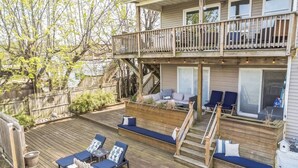 Ein zweistöckiges Haus mit einer Terrasse, Sitzgelegenheiten im Freien und einer Treppe.