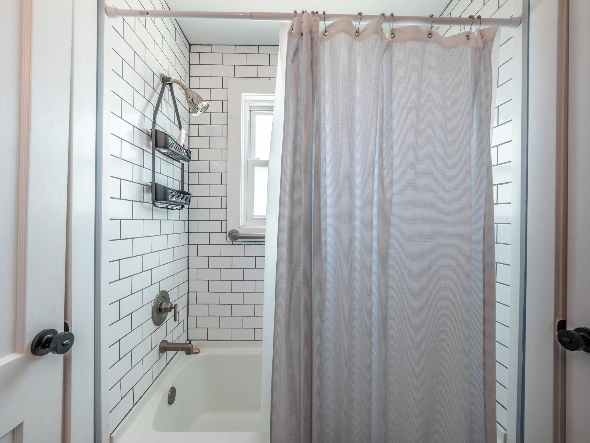 Ein Badezimmer mit weißen Fliesen, einer Badewanne, einer Duschbrause und einem Vorhang.