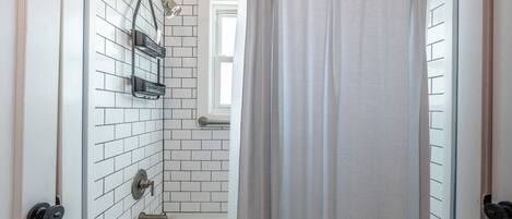 Ein Badezimmer mit weißen Fliesen, einer Badewanne, einer Duschbrause und einem Vorhang.