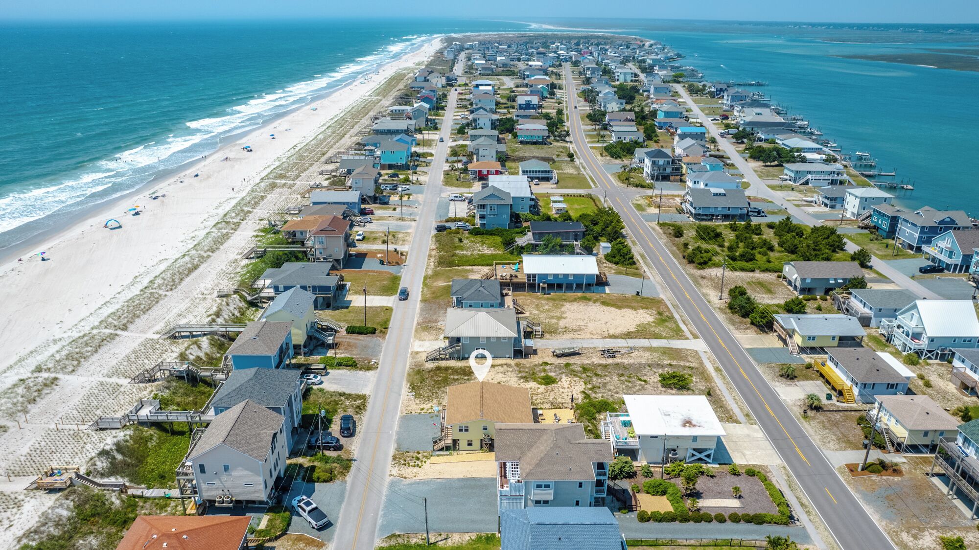 An aerial view of a coastal residential area with houses, a beach, and a marina.