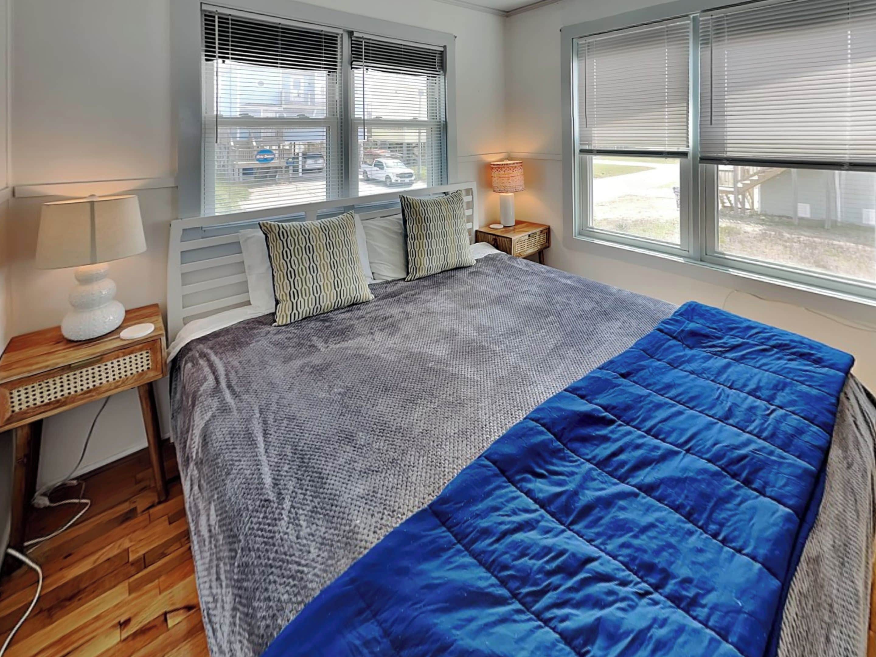 A bedroom with a bed, two bedside tables, a lamp, and a window with blinds.